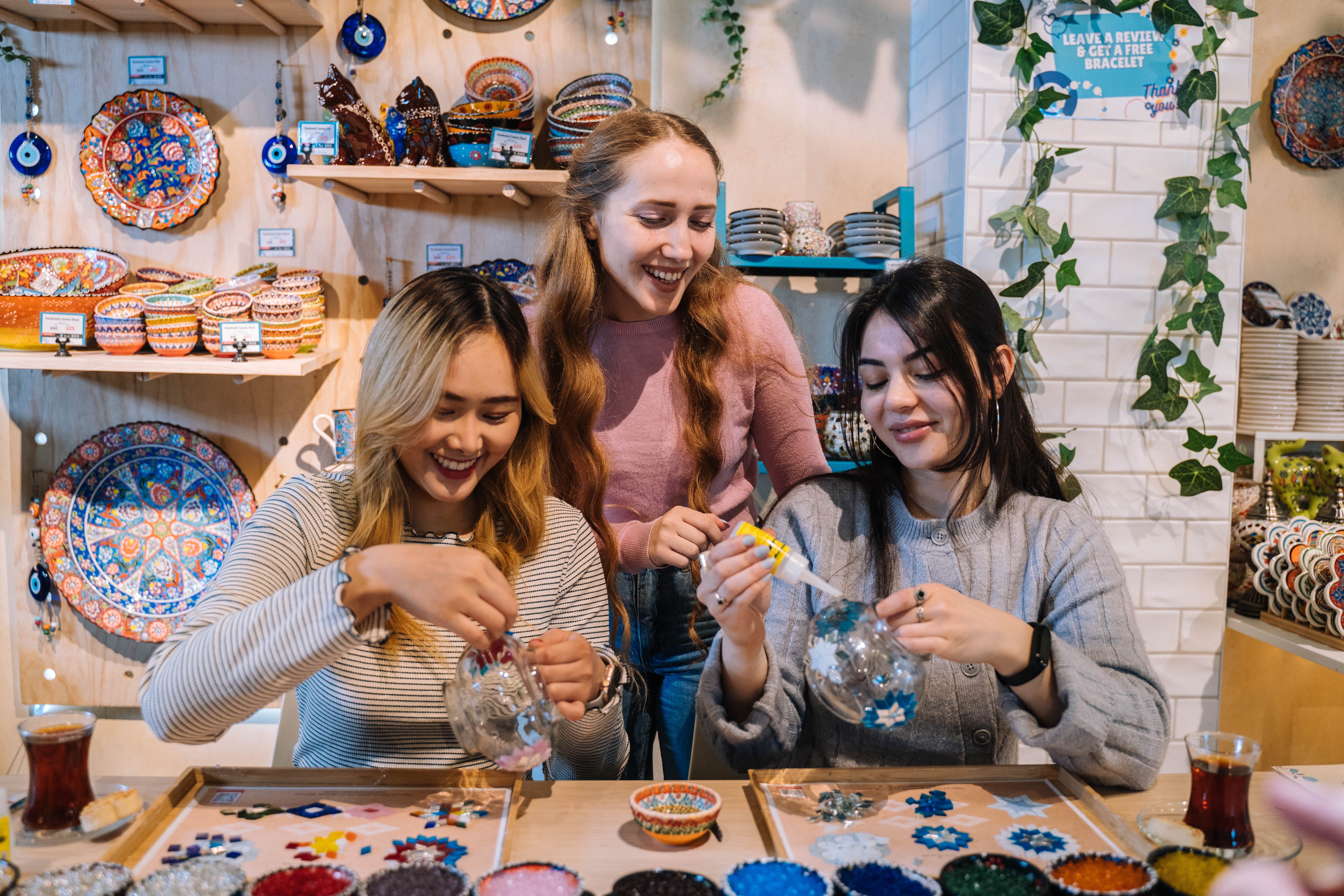 A woman is teaching two other women how to make mosaic lamps